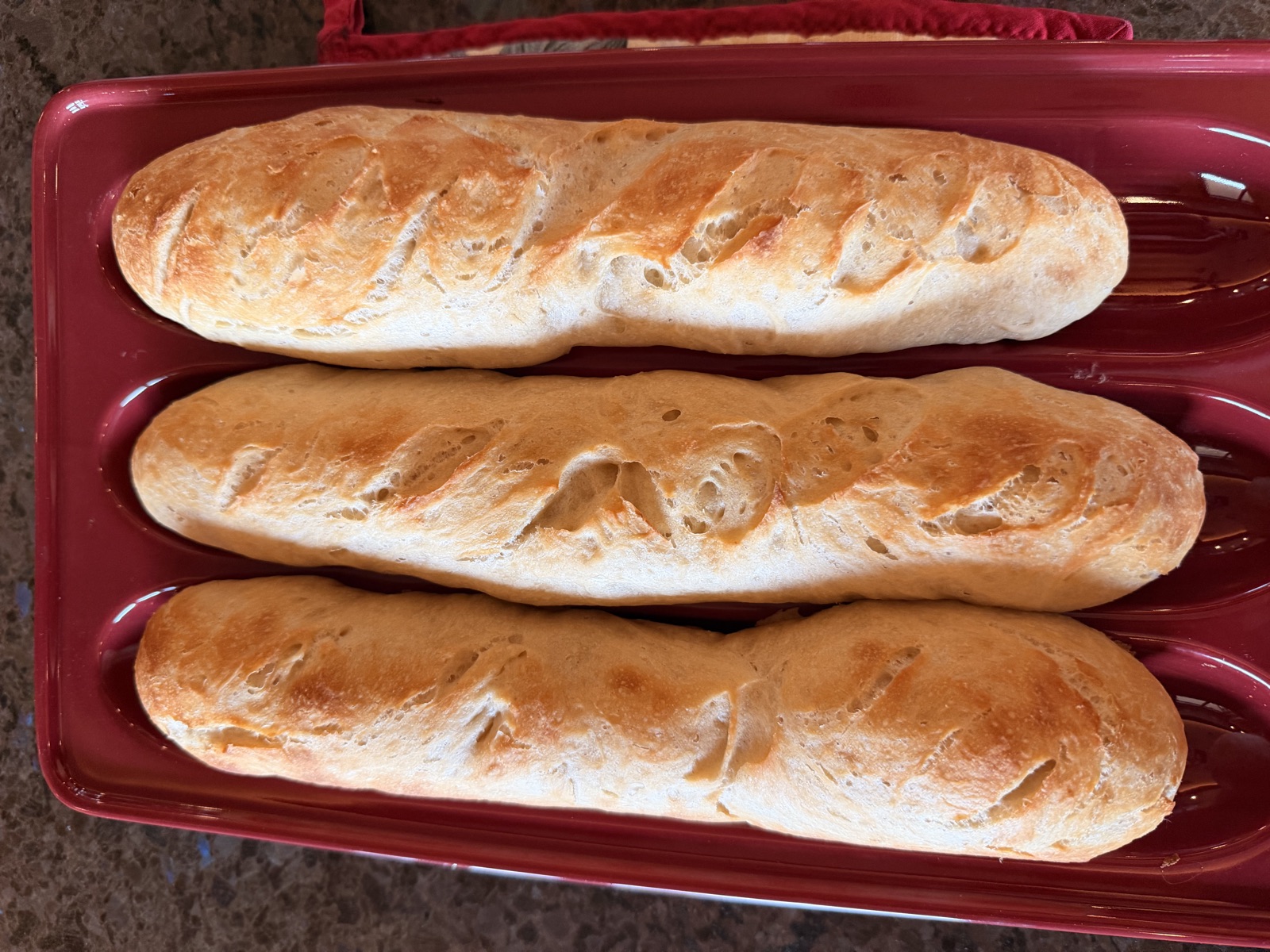 Three golden baguettes fresh from the oven on a red baking tray